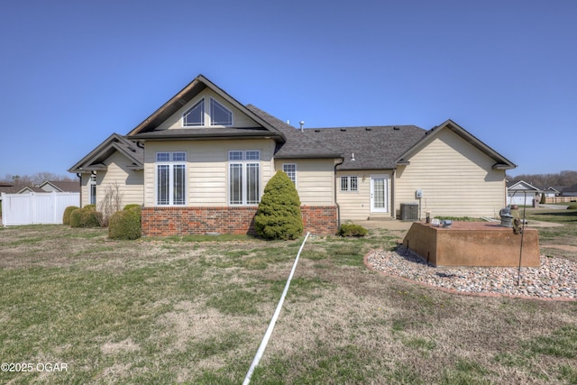 back of property featuring fence, a yard, a shingled roof, brick siding, and central AC unit