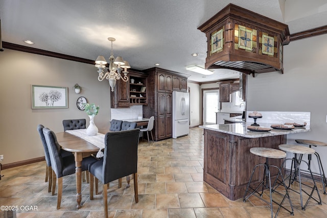 kitchen with an inviting chandelier, a peninsula, freestanding refrigerator, ornamental molding, and dark brown cabinets