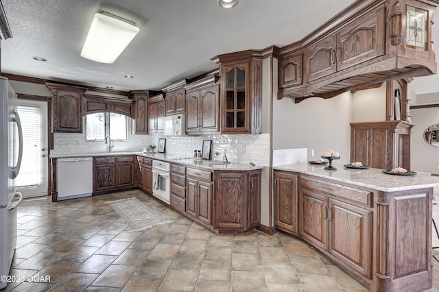 kitchen featuring white appliances, a peninsula, a sink, glass insert cabinets, and tasteful backsplash