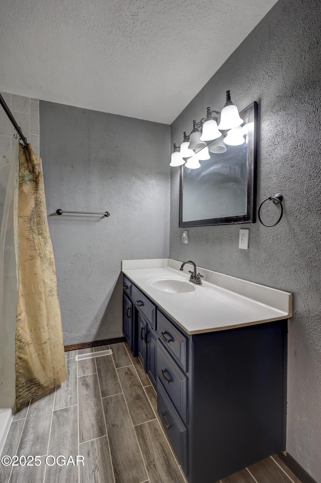 bathroom featuring vanity, a shower with curtain, wood finish floors, a textured ceiling, and a textured wall