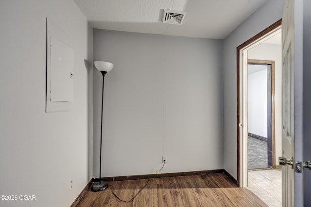 empty room with visible vents, baseboards, light wood-type flooring, electric panel, and a textured ceiling