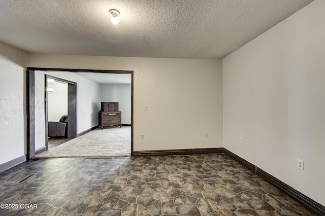 spare room with a textured ceiling, baseboards, and stone finish flooring