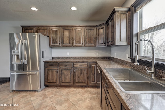 kitchen featuring dark brown cabinetry, dark countertops, stainless steel refrigerator with ice dispenser, and a sink