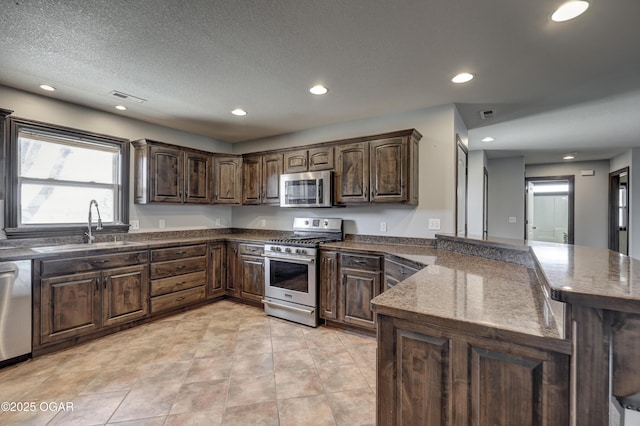 kitchen featuring visible vents, a peninsula, a sink, dark brown cabinets, and appliances with stainless steel finishes