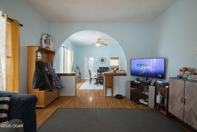 living room with a ceiling fan, wood finished floors, arched walkways, and baseboards