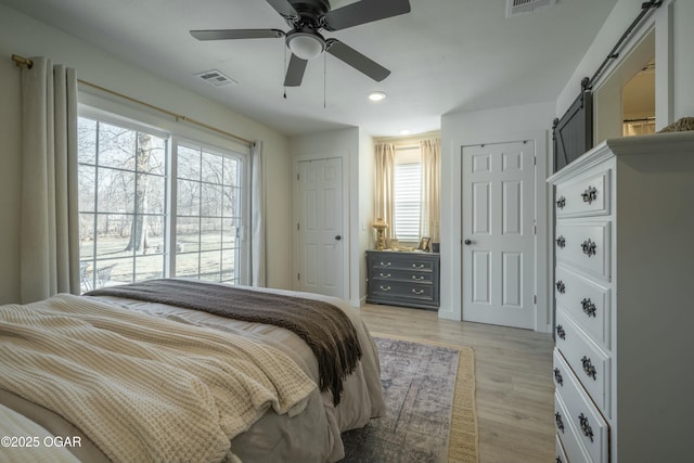 bedroom with a barn door, recessed lighting, visible vents, and light wood finished floors