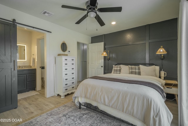 bedroom featuring visible vents, ceiling fan, ensuite bathroom, a barn door, and light wood-type flooring