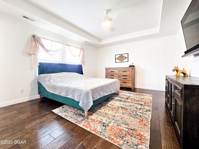 bedroom featuring hardwood / wood-style floors, a ceiling fan, baseboards, visible vents, and a tray ceiling