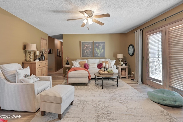 living area featuring visible vents, light wood-style floors, ceiling fan, and a textured ceiling