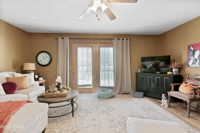 living room with a textured ceiling, ceiling fan, and wood finished floors