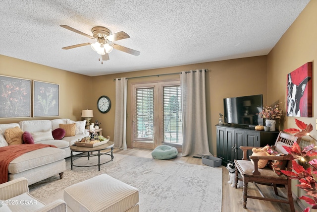 living area featuring a ceiling fan, light wood-type flooring, and a textured ceiling