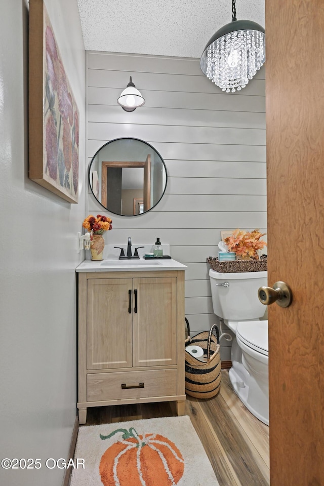 half bathroom featuring a chandelier, toilet, wood finished floors, and vanity