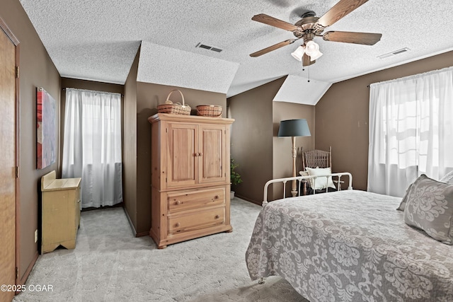 bedroom with a textured ceiling, lofted ceiling, visible vents, and light carpet