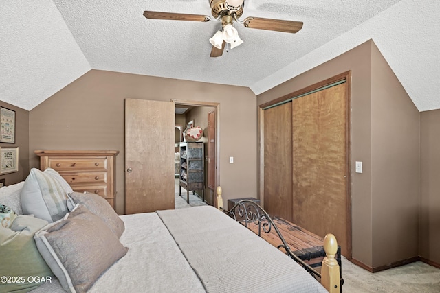 bedroom with lofted ceiling, ceiling fan, a closet, a textured ceiling, and light colored carpet