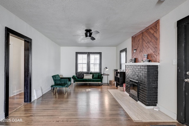 living area featuring visible vents, a brick fireplace, ceiling fan, wood finished floors, and a textured ceiling