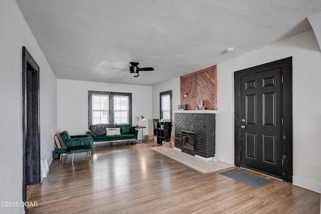 living room featuring a ceiling fan, a textured ceiling, wood finished floors, baseboards, and a brick fireplace