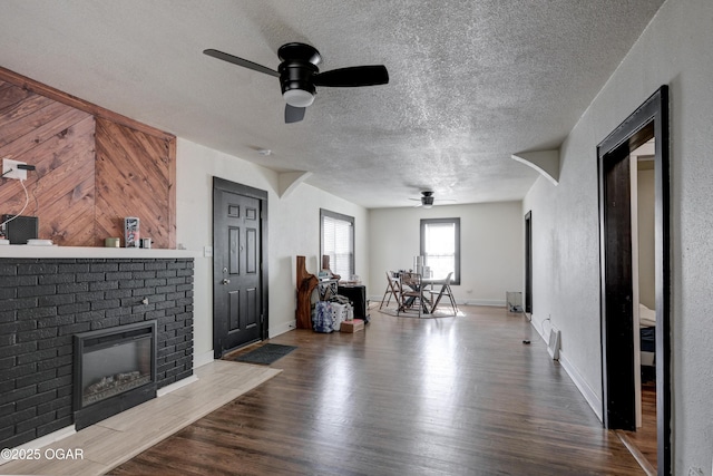 unfurnished living room featuring a fireplace, a textured ceiling, ceiling fan, and wood finished floors