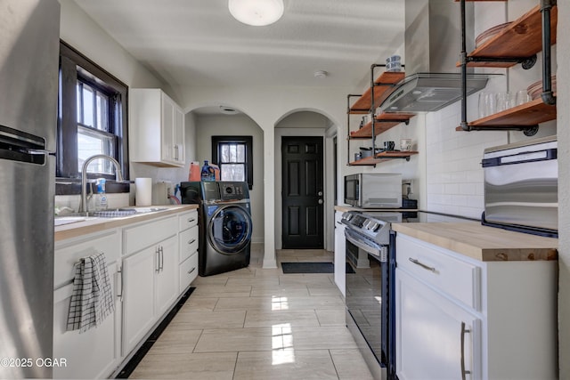 kitchen featuring ventilation hood, washer / dryer, open shelves, a sink, and appliances with stainless steel finishes