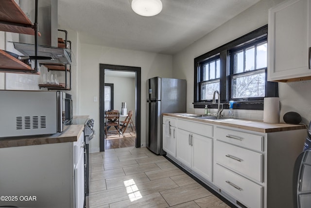 kitchen with wood tiled floor, butcher block counters, freestanding refrigerator, white cabinets, and a sink