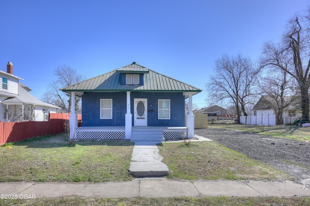 bungalow-style house featuring fence, a standing seam roof, a porch, a front lawn, and metal roof