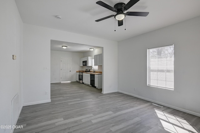 unfurnished living room featuring visible vents, baseboards, light wood-style flooring, and a ceiling fan