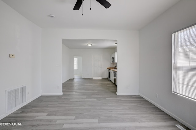 unfurnished living room with a wealth of natural light, visible vents, light wood-style floors, and a ceiling fan