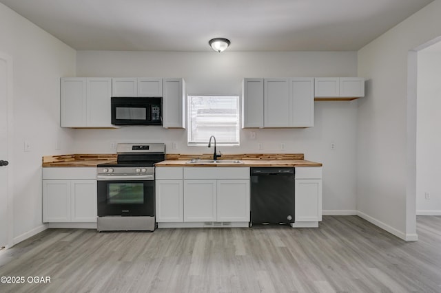 kitchen with black appliances, butcher block countertops, light wood finished floors, and a sink