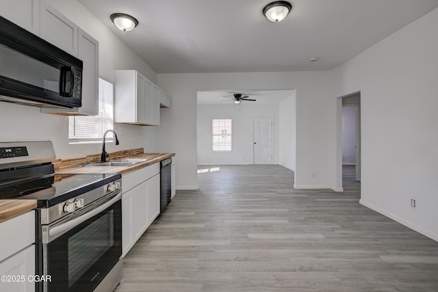 kitchen featuring black appliances, a sink, light wood finished floors, baseboards, and ceiling fan