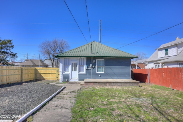 rear view of house featuring a fenced backyard, a lawn, and metal roof