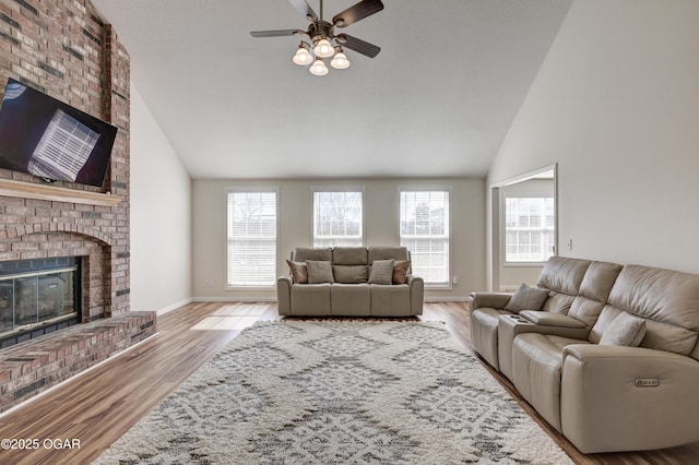 living area featuring high vaulted ceiling, a ceiling fan, wood finished floors, a fireplace, and baseboards