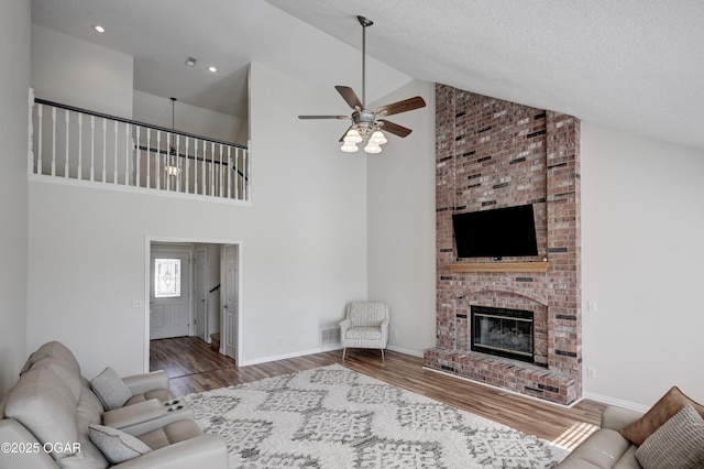 living room featuring wood finished floors, baseboards, visible vents, a ceiling fan, and a fireplace