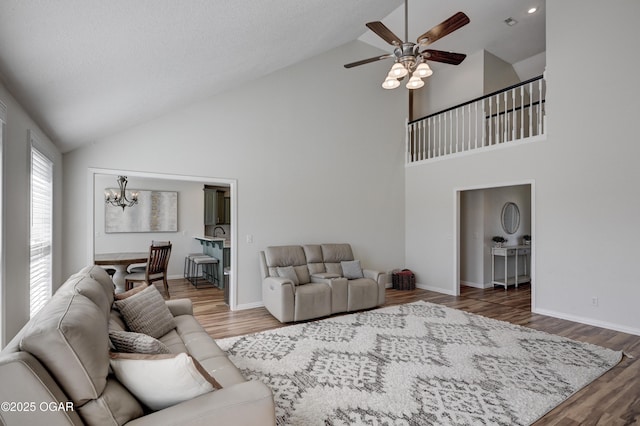 living room with baseboards, ceiling fan with notable chandelier, wood finished floors, and vaulted ceiling