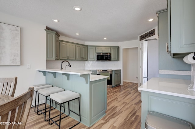 kitchen featuring a kitchen breakfast bar, tasteful backsplash, light wood-style floors, appliances with stainless steel finishes, and light countertops