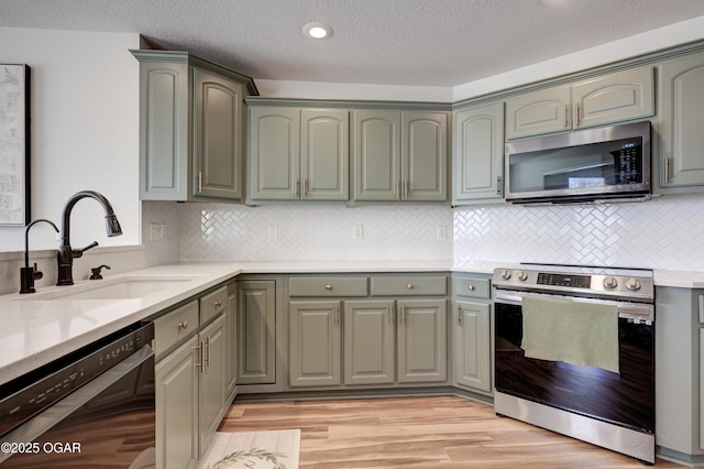 kitchen with gray cabinets, a sink, backsplash, light wood-style floors, and appliances with stainless steel finishes