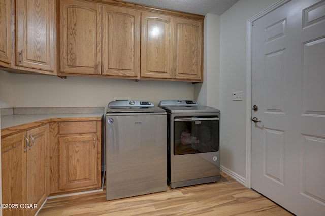 washroom with separate washer and dryer, cabinet space, light wood-style floors, and baseboards