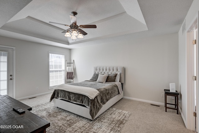 bedroom with light colored carpet, a raised ceiling, a textured ceiling, and baseboards