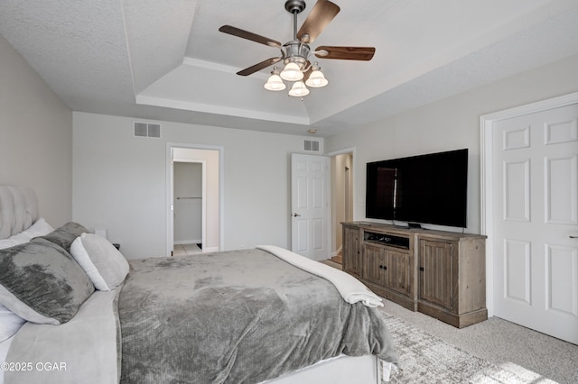 bedroom featuring a tray ceiling, carpet, visible vents, and ceiling fan