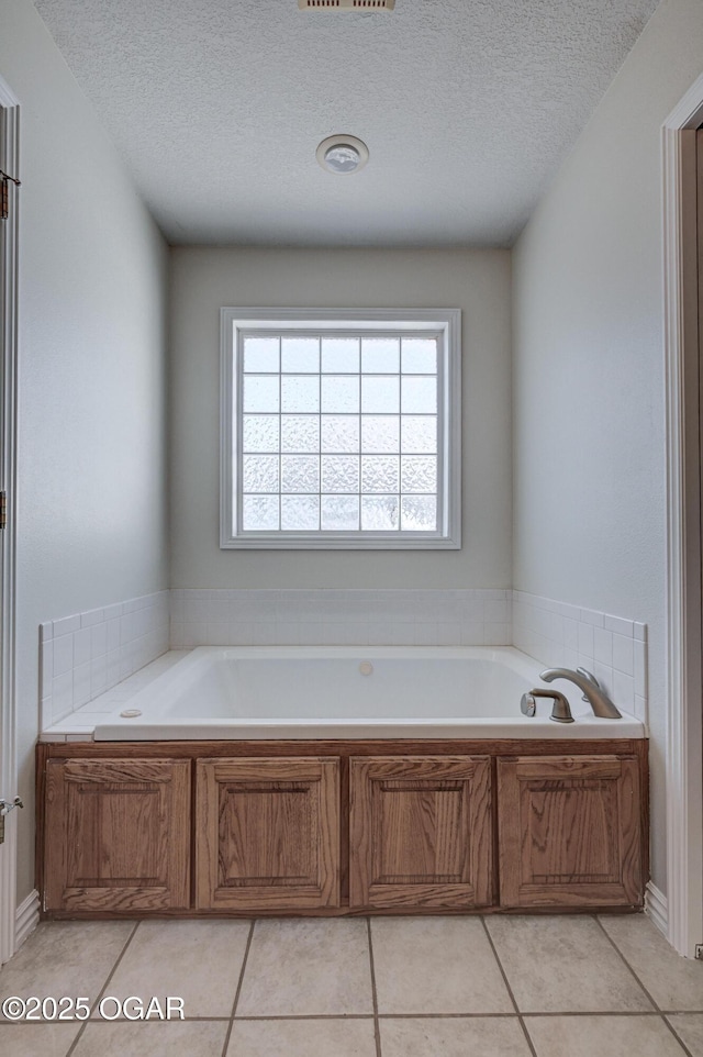 full bath with tile patterned flooring, a bath, and a textured ceiling