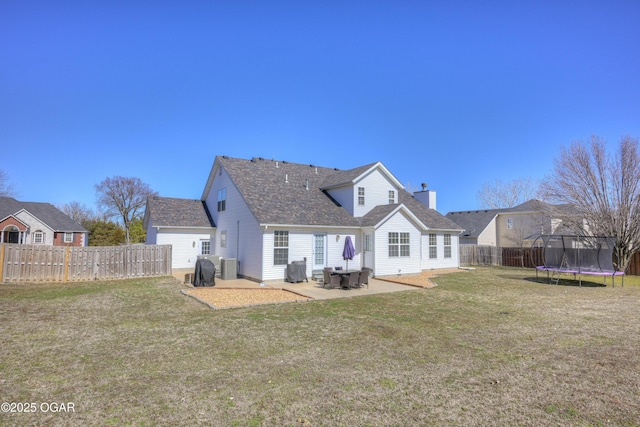 back of property with a patio, a yard, a fenced backyard, a chimney, and a trampoline