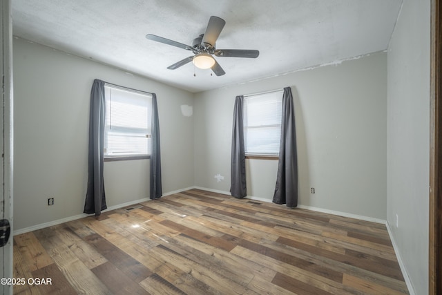 empty room with a ceiling fan, baseboards, and wood-type flooring