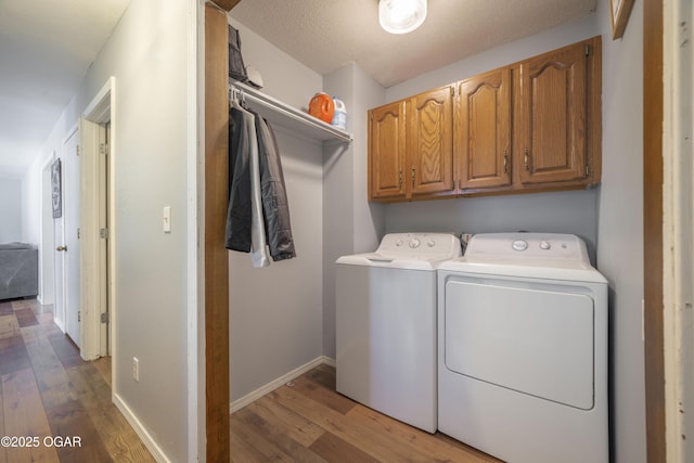 clothes washing area with separate washer and dryer, wood finished floors, cabinet space, and baseboards