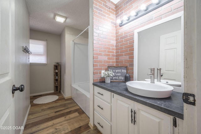 bathroom with a textured ceiling, wood finished floors,  shower combination, baseboards, and vanity