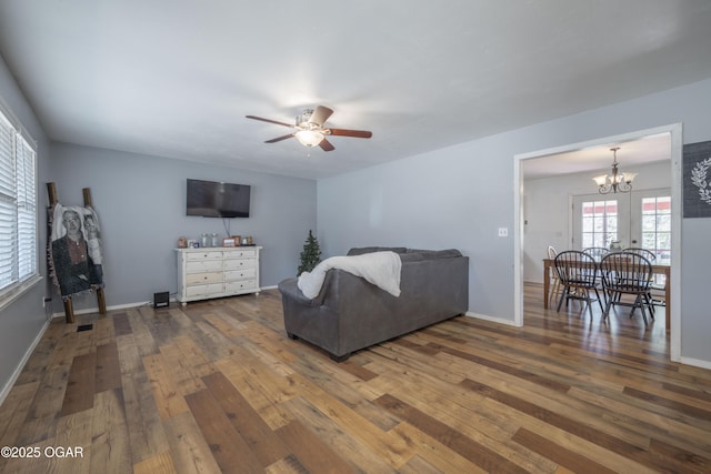 living area featuring baseboards, wood-type flooring, and ceiling fan with notable chandelier