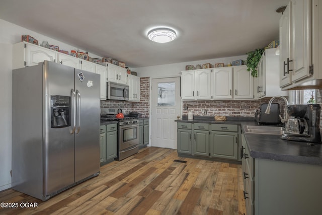 kitchen with dark countertops, backsplash, appliances with stainless steel finishes, light wood-style floors, and a sink