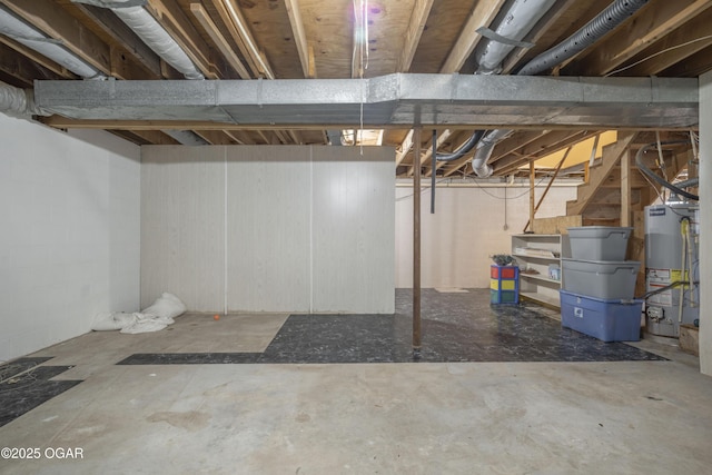 unfinished basement with gas water heater, stairway, and concrete block wall