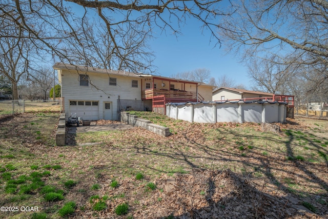 back of property with a covered pool, a wooden deck, an attached garage, and fence