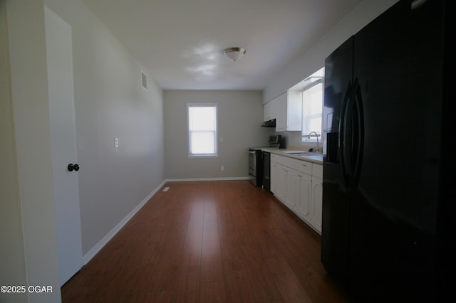 kitchen with dark wood-type flooring, electric range oven, black fridge, white cabinetry, and a sink