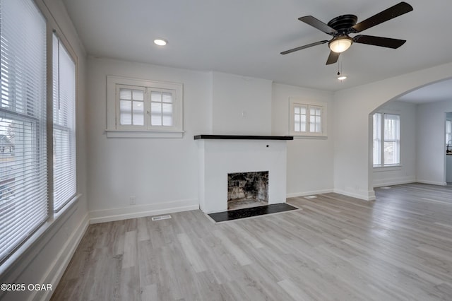 unfurnished living room with visible vents, ceiling fan, a fireplace with flush hearth, wood finished floors, and arched walkways