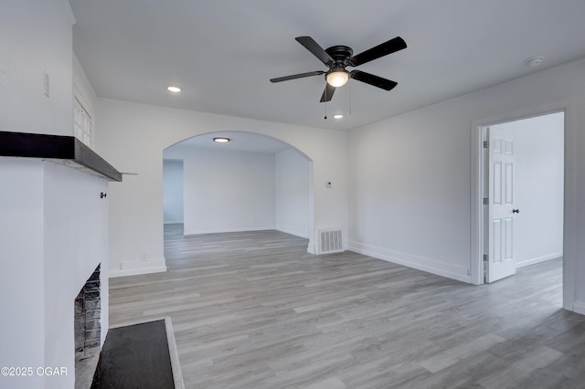 unfurnished living room with visible vents, arched walkways, a ceiling fan, and light wood finished floors