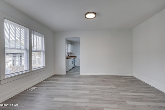 unfurnished room featuring visible vents, light wood-style flooring, baseboards, and a sink